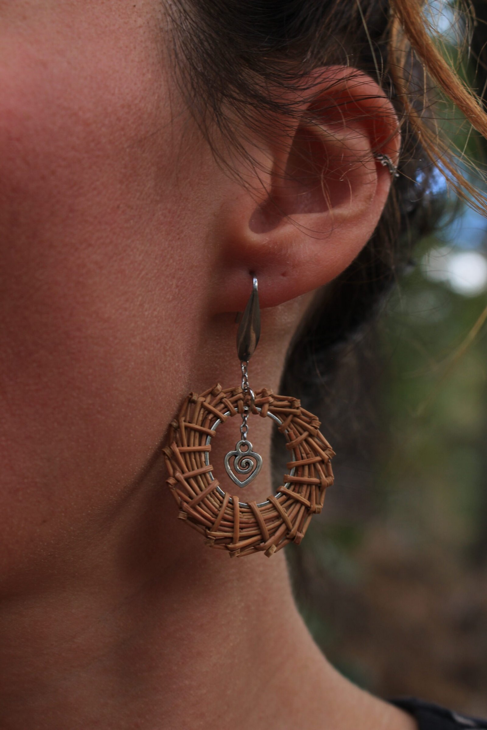 Boucles d’oreilles cœur inox Boucle d’oreille cœur en acier inoxydable argenté et aiguilles de pin laricio, portée à l’oreille, vue de face.