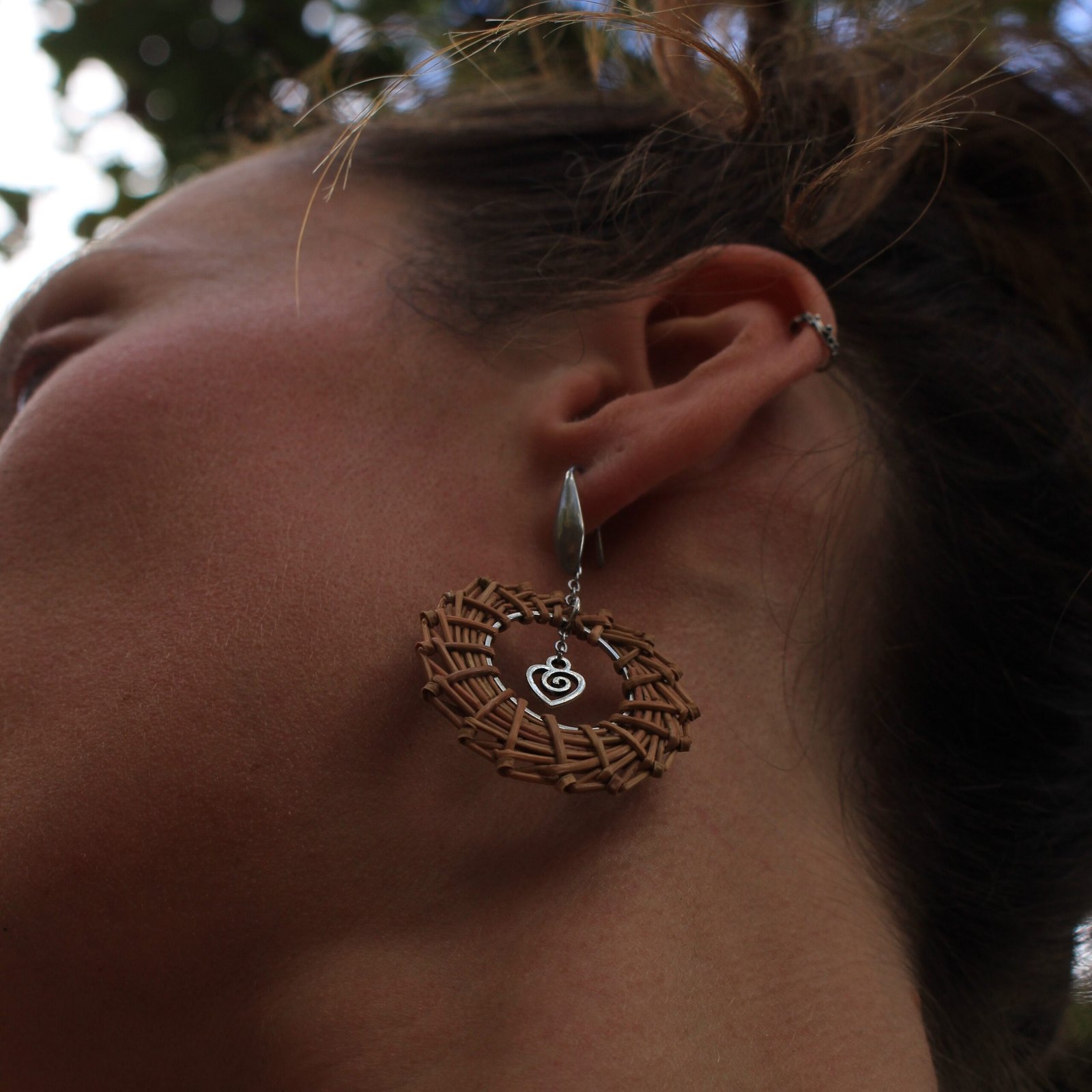 Boucles d’oreilles cœur inox Boucle d’oreille cœur en acier inoxydable argenté et aiguilles de pin laricio, portée à l’oreille, vue du dessous.