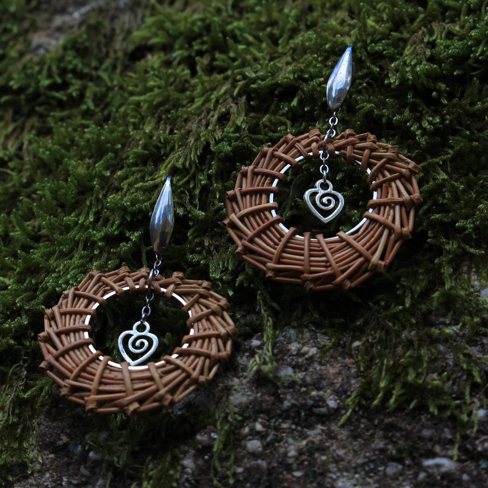 Boucles d’oreilles cœur inox Boucles d’oreilles cœur en acier inoxydable argenté et aiguilles de pin laricio tressées à la main, vues légèrement du dessous.